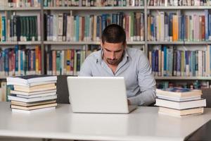 jonge man met laptop in de bibliotheek foto