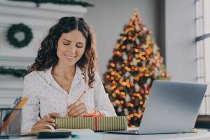 jonge mooie, gelukkige Italiaanse zakenvrouw tekent voorbereide kerstcadeaudoos voor klant op kantoor foto