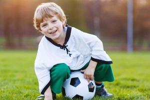 blonde jongen van 4 voetballen met voetbal onl veld foto