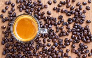 bovenaanzicht van een kop warme espressokoffie met een mooie crema op een houten tafel met gebrande koffiebonen die rondstrooien. focus op een kopje koffie foto