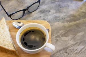 close-up van een kopje warme americano-koffie op een houten dienblad met een broodje op een rustieke betonnen tafel. frisheidsdrankje voor de ochtend. kopieer ruimte foto