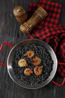 paella van zwarte rijst met garnalen erop. op zicht op houten tafel. foto