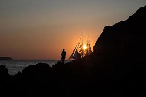 silhouetten van een paar en zeilboot bij zonsondergang