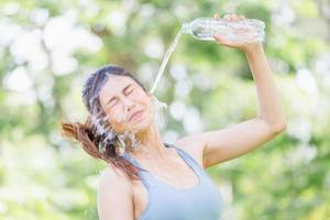 atleet jonge mooie vrouw drinken en opspattend water in haar gezicht in de zomer groen park, sport vrouw drinkwater uit een plastic fles na het sporten foto