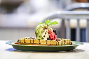zeer smakelijke verse wafel met groene thee-ijs bovenop, versierd met kleine roodbruine witte pop witte chocolade en gelei rode boon naast schijf. foto