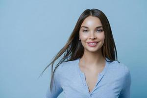 horizontaal schot van mooie vrouw heeft gezond mooi haar, make-up, blij om een nieuwe baan te krijgen, komt op interview, maakt zich klaar om uit te gaan voor een romantische date, kijkt direct naar de camera, poseert binnen foto