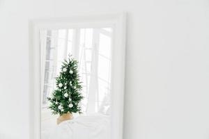 versierde kerstboom weerspiegelt in spiegel, witte ruime kamer. slaapkamer met nieuwjaarsdecoratie. moderne klassieke stijl. kerstavond thuis foto