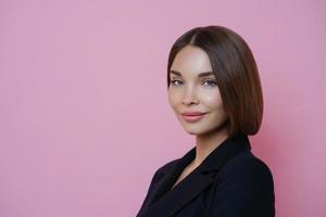 profielfoto van een donkerharige vrouw gekleed in een zwart pak, heeft natuurlijke make-up, ziet er zelfverzekerd uit binnen, poseert tegen een roze achtergrond, lege ruimte voor uw promotie. vrouwen en elegantie concept foto