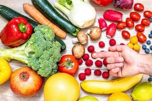 hand met voedingssupplementen boven groenten en fruit voor een gezonde levensstijl foto