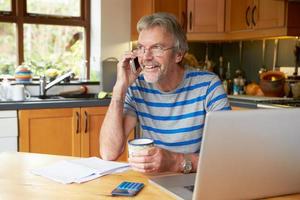 volwassen man met behulp van mobiele telefoon thuis financiën kijken foto