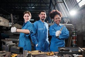 multiraciale industriearbeiders in veiligheidsuniformen werken samen met eenheid, handelen met gereedschap en uiten gelukkig werk samen met een glimlach en vrolijk in mechanische fabriek, professionele ingenieursbezetting. foto
