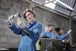 jonge blanke vrouwelijke industriearbeider werkt met precisiegereedschappen voor metaalbewerking, draaibankmachines en werkplaats voor reserveonderdelen met een multiraciaal team in de productiefabriek, professionele werktuigbouwkundigen. foto