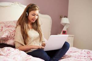 tienermeisje liggend op bed met behulp van laptop hoofdtelefoon dragen