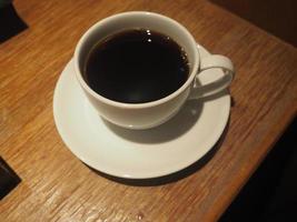 rook op zwarte koffie in een witte kop op een houten tafel foto