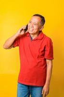 portret van gelukkige Aziatische senior man praten over de telefoon en glimlachend geïsoleerd over gele achtergrond. foto