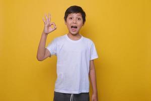 Aziatische jongen in een casual stijl met ok teken op een gele achtergrond. het concept van succes, goedkeuring. mock-up voor kindermode. foto