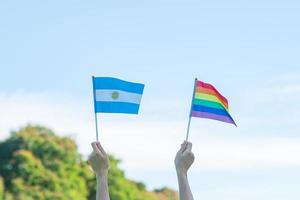 handen die lgbtq-regenboog en de vlag van Argentinië op aardachtergrond tonen. ondersteuning van lesbische, homoseksuele, biseksuele, transgender en queer gemeenschap en het concept van de trotsmaand foto