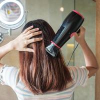 jonge vrouw met föhn in de buurt van spiegel thuis of hotel. kapsels en lifestyle concepten foto