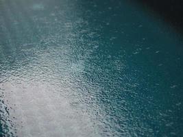 regendruppels vallen blauw water in het zwembad achtergrond rimpelingen op de oppervlaktetextuur, glinsterende bokeh abstract foto