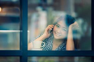 Gelukkige vrouw Azië praten telefoon in café en genieten van koffie foto