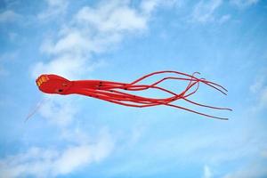 felrode roze octopusvlieger die in blauwe lucht vliegt met wolken, rode octopusvormige vlieger, vliegerfestival foto