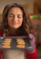 gelukkige jonge huisvrouw genieten van geur van kerstkoekjes op pan