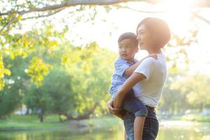 mooie jonge aziatische moeder met kleine jongen in het park, aziatische vrouw blij met zoon en knuffelkind, moederliefde en omarmen kind samen in de zomer, moederdag en familieconcept. foto