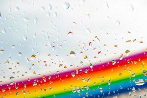 een regenboog achter een glazen ramen met waterdruppels, oogpunt, van achter het glas met druppels. foto