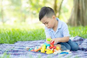 kleine jongen speelt voor idee en inspiratie met speelgoedblok in het grasveld, kind leert met bouwblok voor onderwijs, kinderactiviteit en spel in het park met gelukkig in de zomer. foto