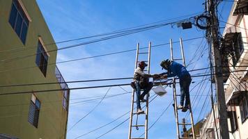 lage hoekmening van 2 technici op houten ladder werken aan het installeren van telefoondraden op elektrische paal tegen de oude gevel en blauwe hemelachtergrond foto