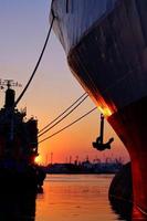 silhouet deel van voorwaartse en achterwaartse vrachtschepen met anker en meertros die aanmeerden in de haven tegen de achtergrond van de zonsonderganghemel in de avondtijd en verticaal frame foto