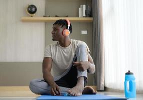 jonge afrikaanse man ontspannen, naar muziek luisteren na het beëindigen van yoga-oefening in de woonkamer van het huis foto