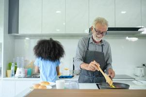 familievakantie-activiteiten met opa en kleinkinderen. samen eten koken voor de familie grootvader geeft kookles aan zijn half-Aziatische kleindochter Afro-Amerikaan foto