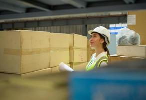 vrouwelijke magazijnmedewerker die artikelen telt in een industrieel magazijn op de tussenverdieping van de fabriek. dat is een opslag voor kleine en lichte elektronische onderdelen. foto