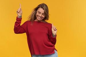 studio shot van vrolijke opgewonden jonge vrouw in terracotta sweatshirt dansen en omhoog wijzend over gele achtergrond. ziet er gelukkig uit foto