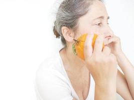 negenenveertig jaar oude vrouw in een wit t-shirt tegen een witte achtergrond met een sinaasappel foto