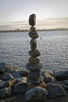 de kunst van het balanceren van rotsen met water, wolken en lucht op de achtergrond foto