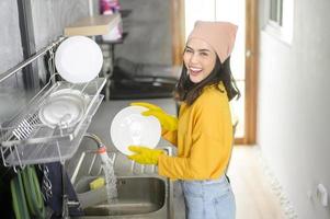 jonge gelukkige vrouw die gele handschoenen draagt die thuis afwassen in de keuken foto