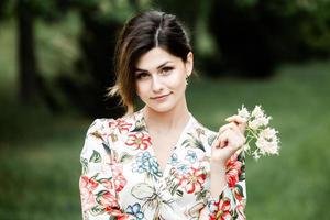 vrouwenportret met een haar dat in de wind beweegt. portret van jonge mooie Russische brunette meisje in zomer groen park. Europese blanke vrouw in jurk. foto