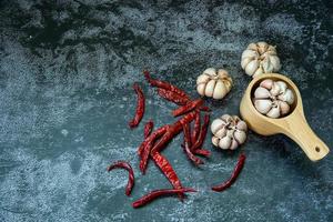 rode gedroogde hete chili peper en knoflook in houten lepel op grijze textuurachtergrond, chili en knoflook zijn onderdeel van Thais eten foto