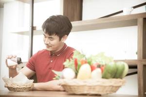 Aziatische glimlachende jonge man met casual rood t-shirt geniet van ontbijten, frietjes eten, jonge man koken in de keukenkamer in loftstijl foto