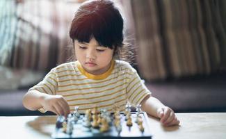 kleine Aziatische baby schaken in de woonkamer thuis. slimme kid.fashion kinderen. klein geniaal kind. intelligent spel.schaakbord. baby activiteit concept. foto