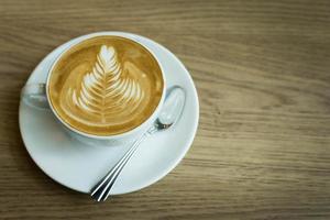 hete kunst latte koffie in een beker op houten tafel foto