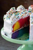 plakje vrolijke regenboogcake met wit glazuur en hagelslag foto