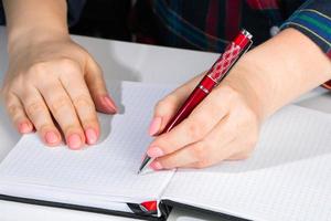 vrouw schrijft in een notitieboekje en houdt een pen vast met haar linkerhand. het meisje werkt op kantoor. linkshandigen dag 13 augustus. foto