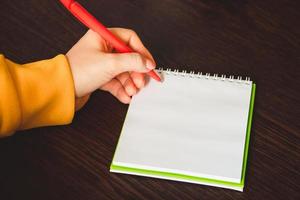 linkshandigen dag. zakenvrouw schrijft een notitie in notitieblok. meisje houdt een pen in haar linkerhand close-up. foto