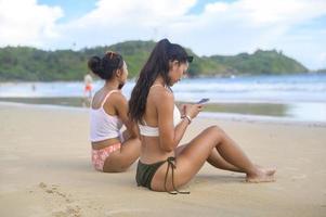 jonge mooie vrouw in bikini luisteren naar muziek en het gebruik van smartphone op het strand, zomer, vakantie, vakantie, levensstijl concept. foto