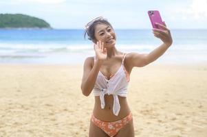 jonge mooie vrouw in bikini luisteren naar muziek en het gebruik van smartphone op het strand, zomer, vakantie, vakantie, levensstijl concept. foto