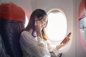 jonge mooie vrouw gebruikt smartphone op vliegtuig-, reis- en vakantieconcept foto