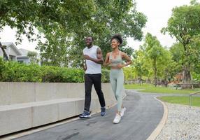 man en vrouw blij joggen in groene tuin. vrolijke jonge paar lachende oefening in de avond zomer. Afro-Amerikaanse familie geniet ervan om samen buiten in het park te rennen. gezonde levensstijl. foto